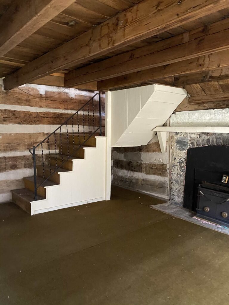 A set of stairs, leading down into a small room, a brick fireplace is visible